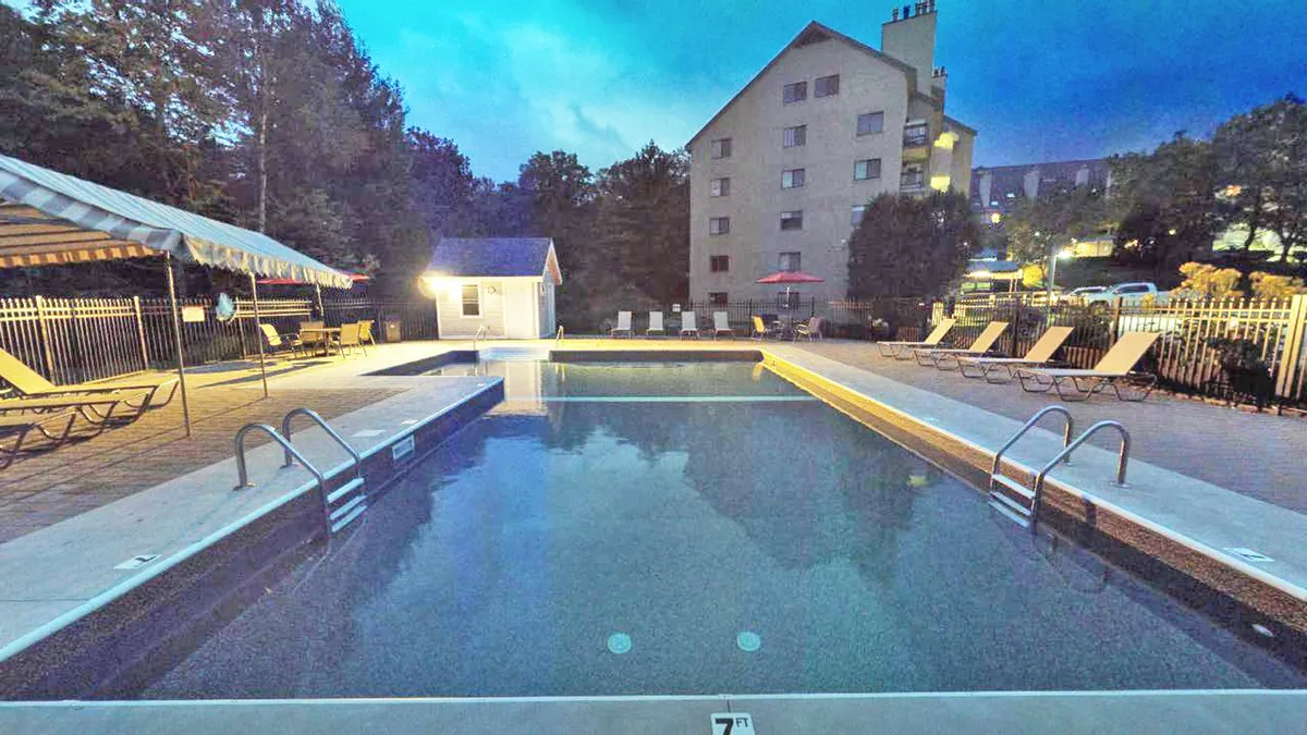 An inviting exterior pool area with loungers and a canopy, set against the backdrop of the main building. The tranquil blue water reflects the evening sky, while the seating areas suggest relaxation and socializing after a day outdoors.