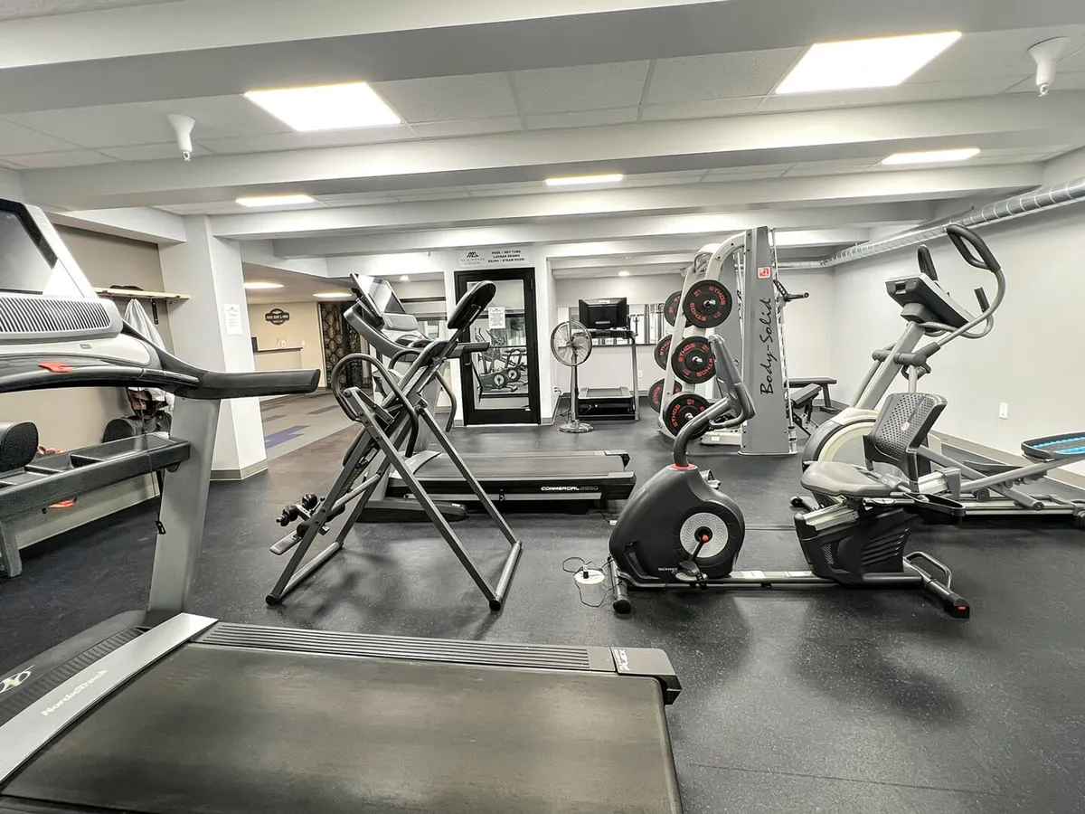 A well-equipped fitness center featuring treadmills, an elliptical machine, weightlifting equipment, an exercise bike, and a television. The space appears bright and functional, designed for guests focusing on their health and fitness routines.
