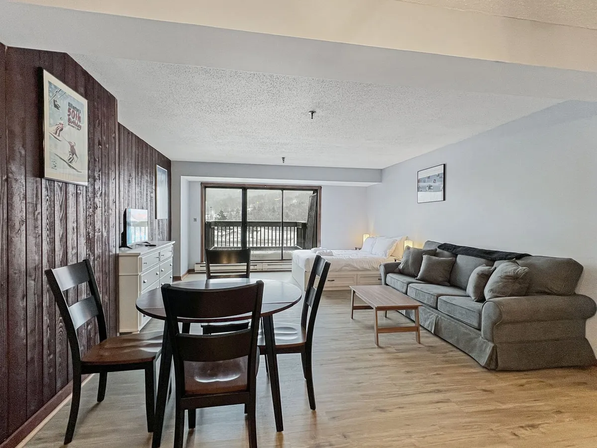 A cozy living area featuring a comfortable sofa, a dining table, and large windows with a panoramic view of the mountains. The natural light streams in, creating a bright and airy ambiance.