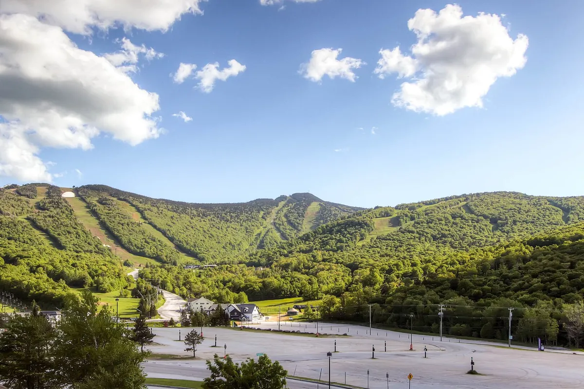 A sweeping view of lush green mountains and a clear blue sky, offering a visual sense of the natural scenery surrounding Killington. The focus is on the pristine landscape, with no man-made structures in sight, inviting thoughts of hiking and mountain biking adventures.