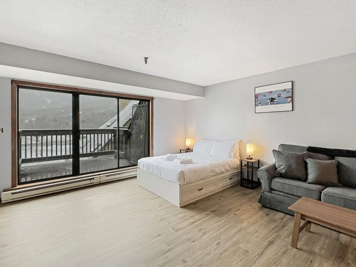 This image showcases a serene studio interior with a plush sofa, a neatly made double bed, and a large window that frames breathtaking views of Killington Peak. The space is filled with natural light, and the arrangement creates an inviting atmosphere for relaxation or enjoying the scenery.